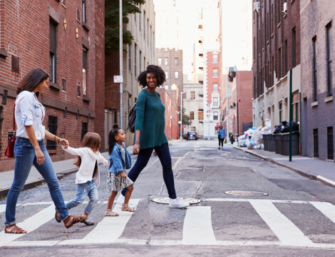 Two moms smile at their children while they all are crossing a crosswalk